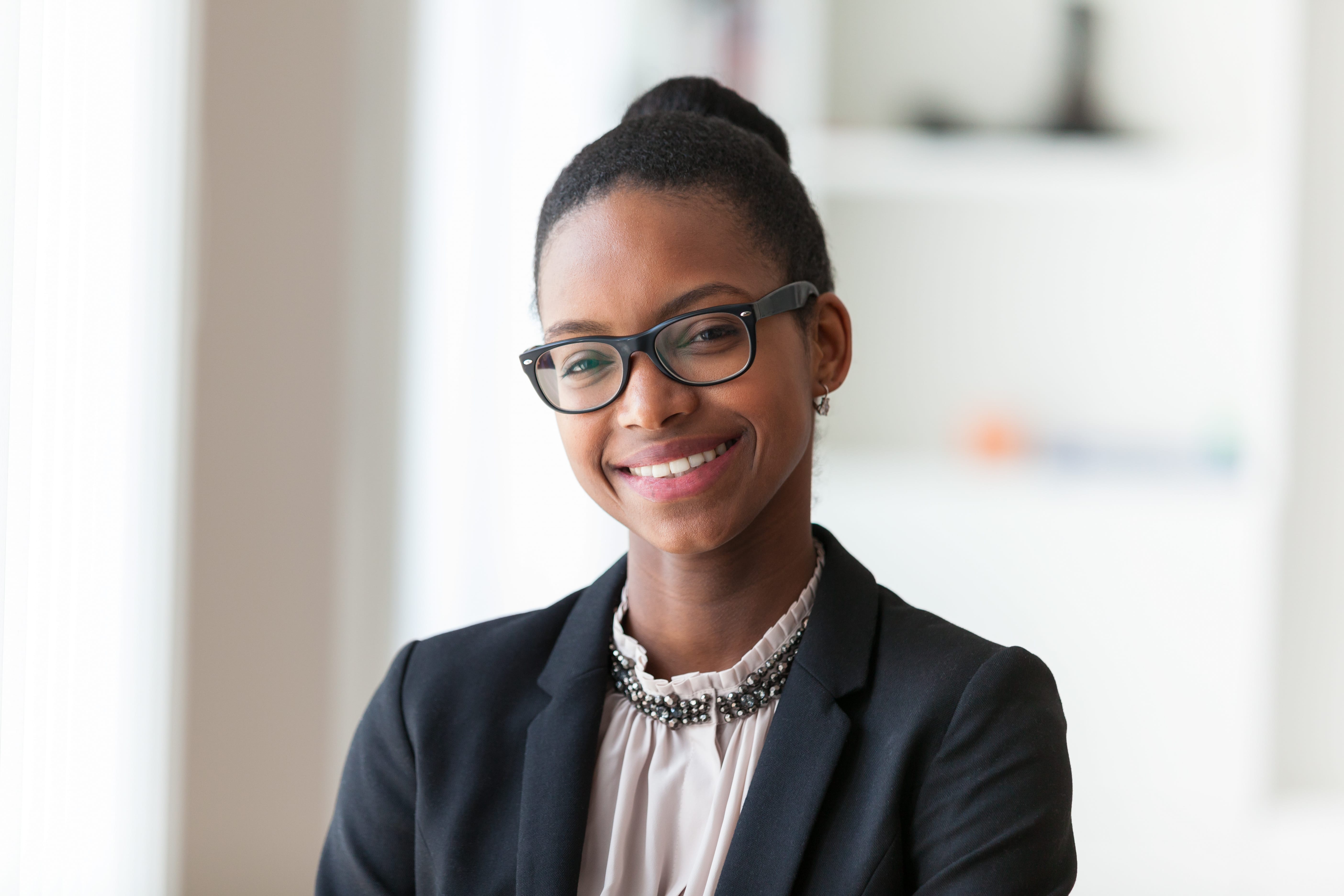 Professional headshot of a woman in a black blazer and glasses — bright natural light background