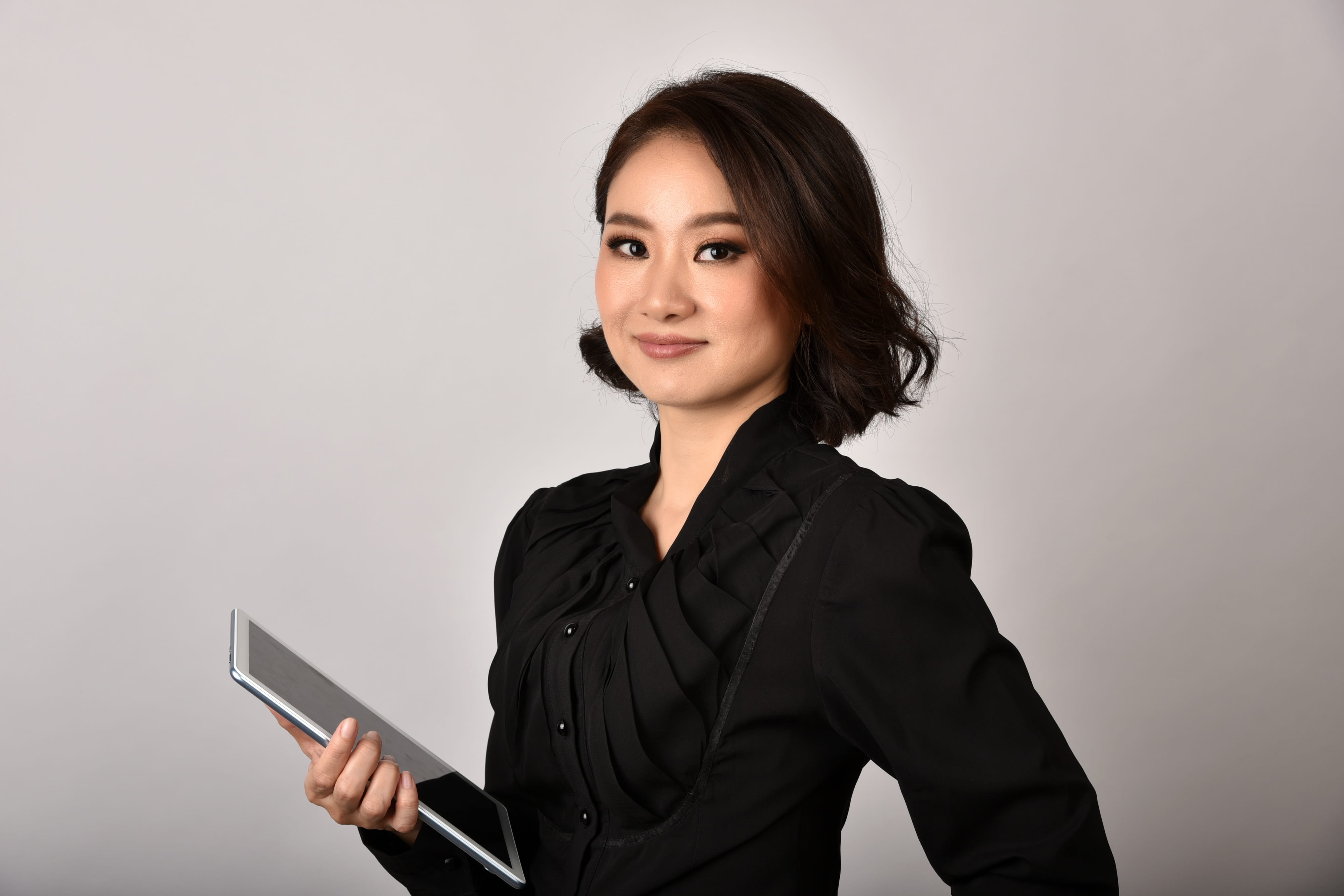 Professional headshot of a woman in a black blazer holding a tablet — clean studio background